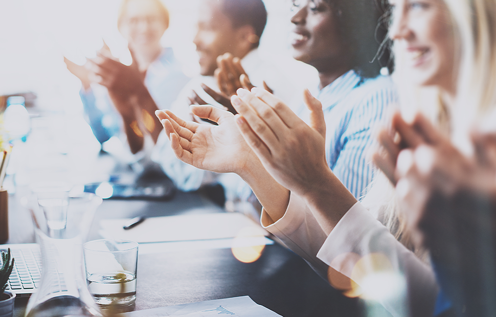 A slightly blurry image of people clapping to show appreciation, with glasses placed in front of them on a table.