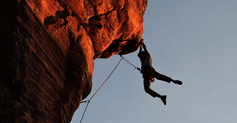 A photo of a person hanging off the side of a mountain with safety ropes attached.