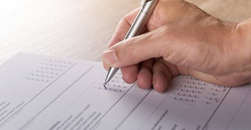 A photo of a person answering multiple choice questions on paper with a black pen.