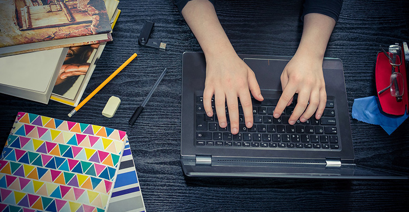 An overhead shot of a person typing on his laptop with various stationery objects on the table.