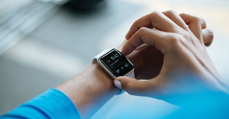 An overhead photo of a person wearing a blue sweater is seen adjusting their smartwatch.