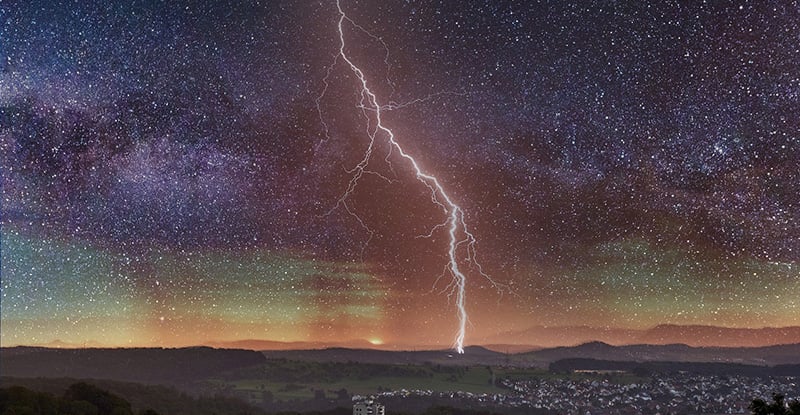 A photo of a lightening striking in the distance on a clear starry night.