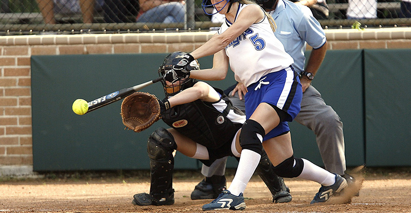 A photo of a woman hitting a ball with a baseball bat at a tournament.