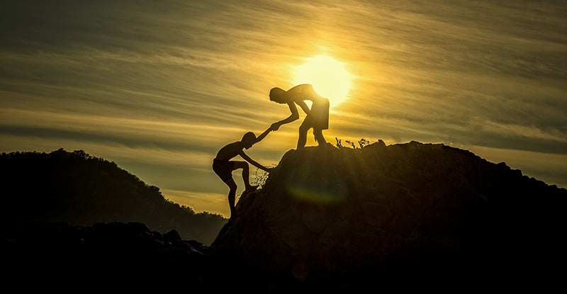 A photo of a person giving a hand to another person to climb the top of a mountain.