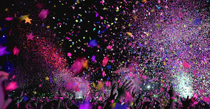 A photo with people gathered and throwing confetti and glowing stars in the air.