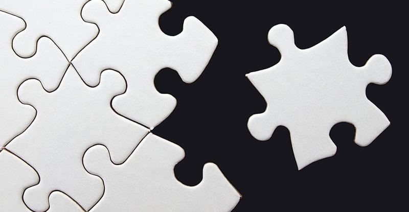 A photo of white puzzle pieces on a black background with only one puzzle piece set aside.