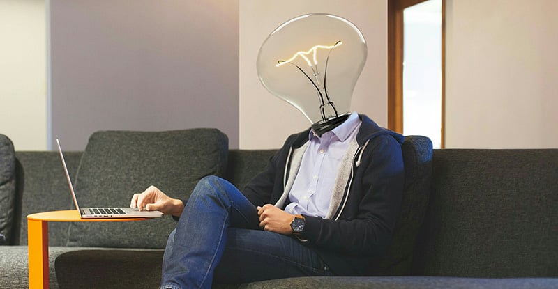 A photo of a person typing on a laptop but the head is replaced by a light bulb.