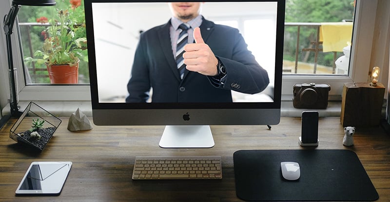 A photo of a desktop with a man on the screen showing thumbs up.