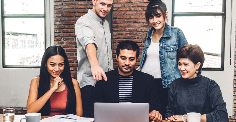 A photo of a group of students working together on one laptop with one student pointing at the laptop.