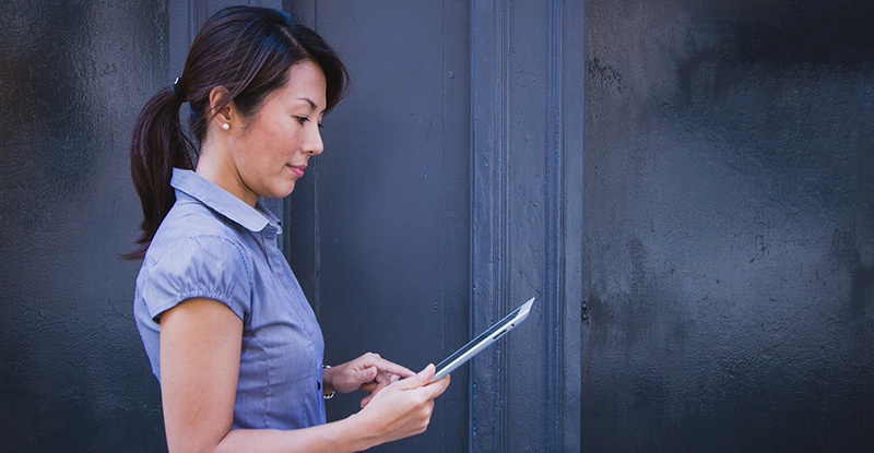 A photo of a side profile of an Asian woman reading something on her tablet.