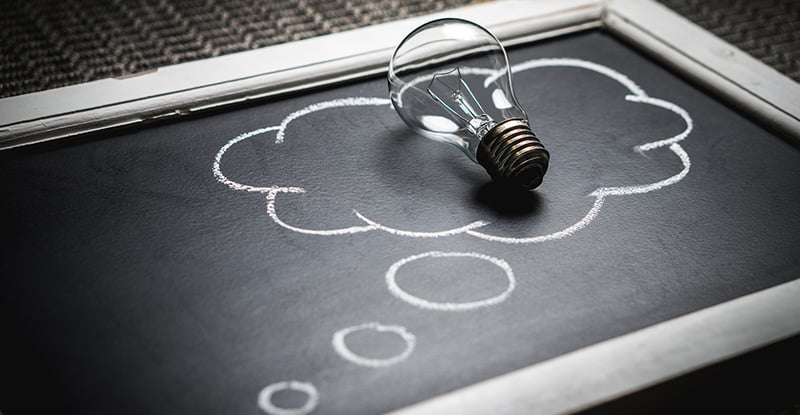 A photo of a black slate with a cloud drawn on it and a light blub is placed on the cloud.