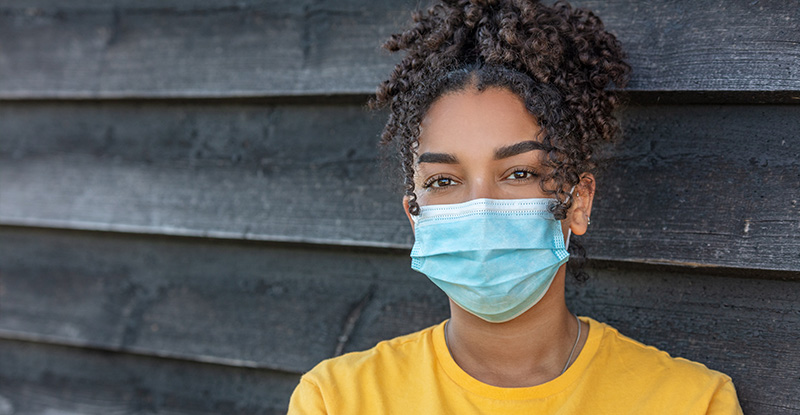 A photo of an African descent woman wearing a face mask and looking directly at the camera.