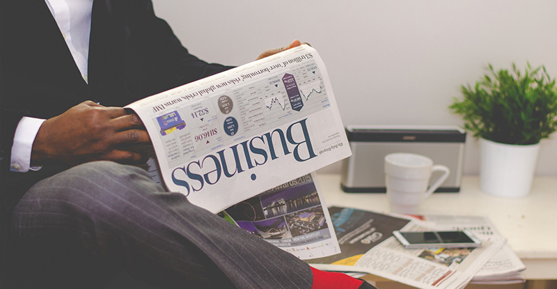 A photo of a business man seated in a couch reading the Business newspaper.