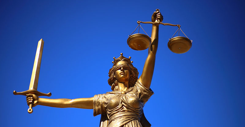 A photo of a bronze statue of Lady Femida taken from a low angle against a clear blue sky.