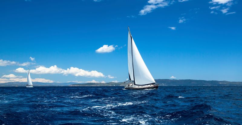 A photo of two sailboats gliding on the sea under a clear blue sky, capturing a serene and peaceful moment.