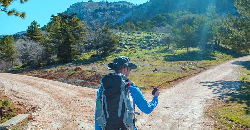 A photo of a man hiking with a digital compass is standing at a crossroads, trying to figure out which way to go.