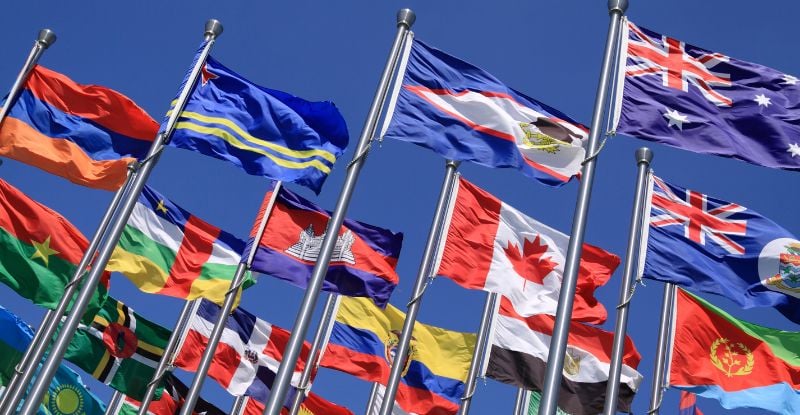 A photo of multiple country flags against a backdrop of clear blue skies.