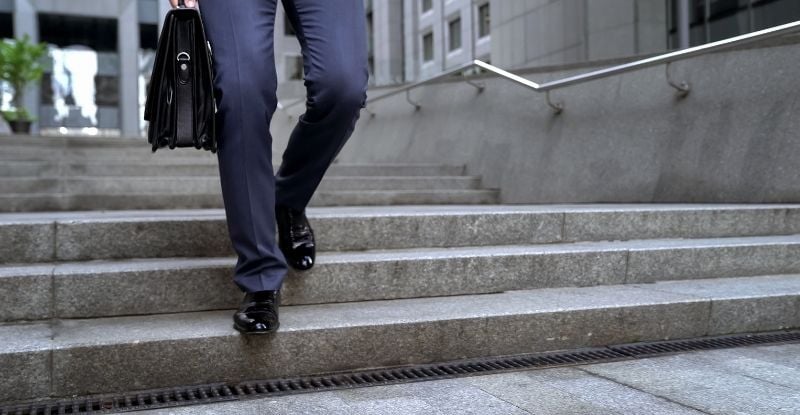 A photo of a man with a brief case climbing down the stairs outside an office building.