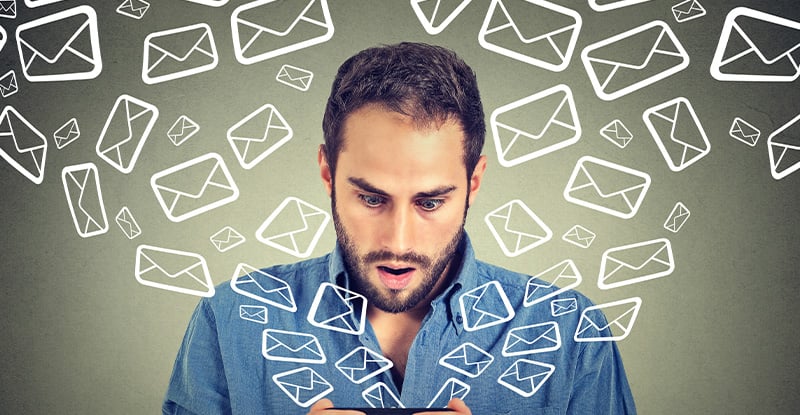 A photo of a man looking surprised while holding a phone in his hand. Message icons are flying out of the phone, symbolizing him receiving numerous messages.