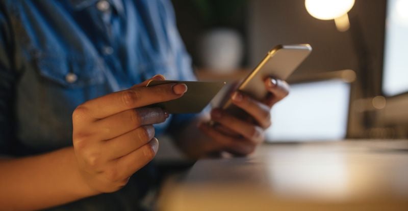 A photo of a person holding a credit card in one hand and a phone in the other.