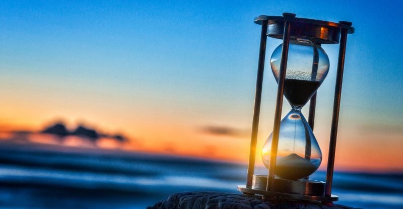 A photo of an hourglass placed on a rock, with a serene background of the sea and a vibrant sunset, symbolizing the passage of time.