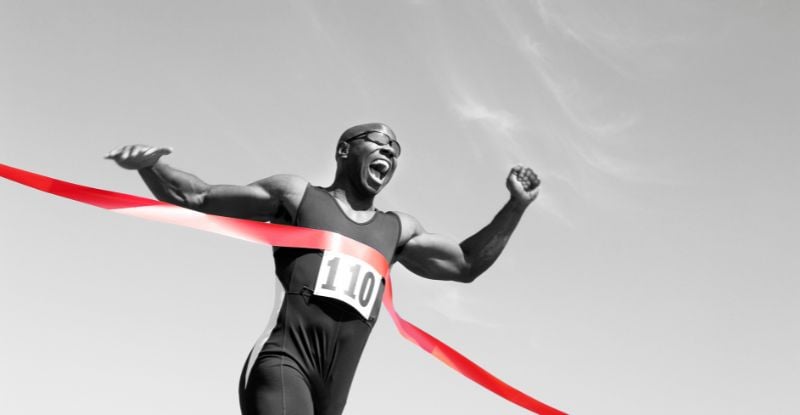 A black and white photo of an African man winning a race. The ribbon is in red colour.