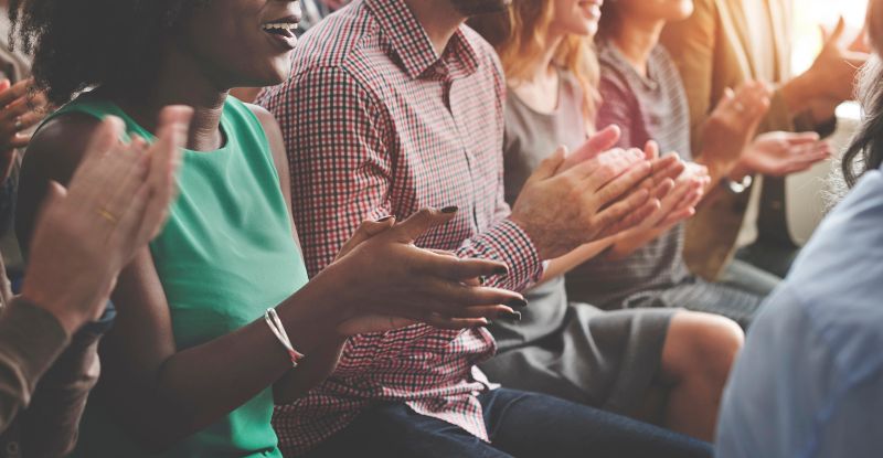 A photo of a group of people clapping their hands in celebration.