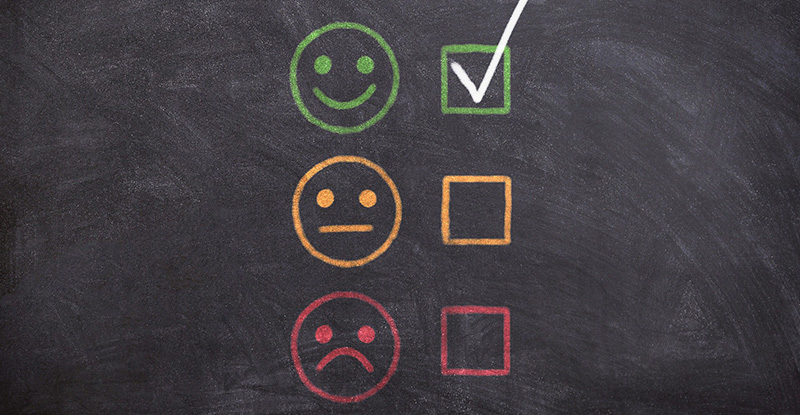 A photo of a blackboard displaying smiley faces representing satisfaction levels—happy, neutral, and sad. The happy face is marked to indicate satisfaction.